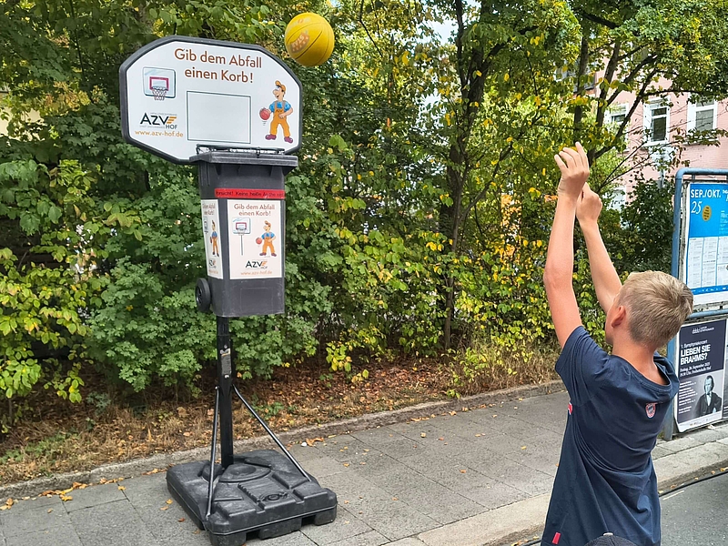 Ein Junge wirft einen Ball in einen Basketballkorb mit der Aufschrift "Gib den Abfall einen Korb"