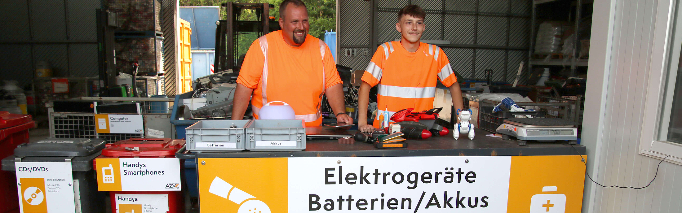 An der Theke für Annahme von Elektrogeräten am Wertstoffhof Hof stehen zwei Mitarbeiter