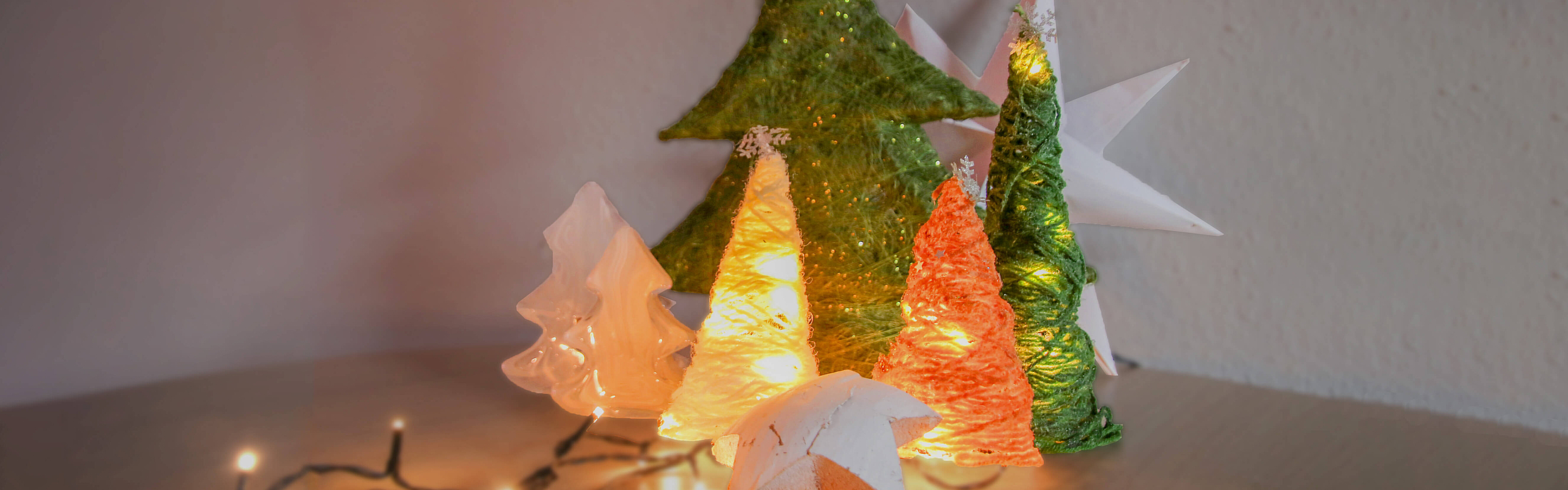 gebastelter Weihnachtsbäume aus Wollresten mit Lichterketten dekoriert.